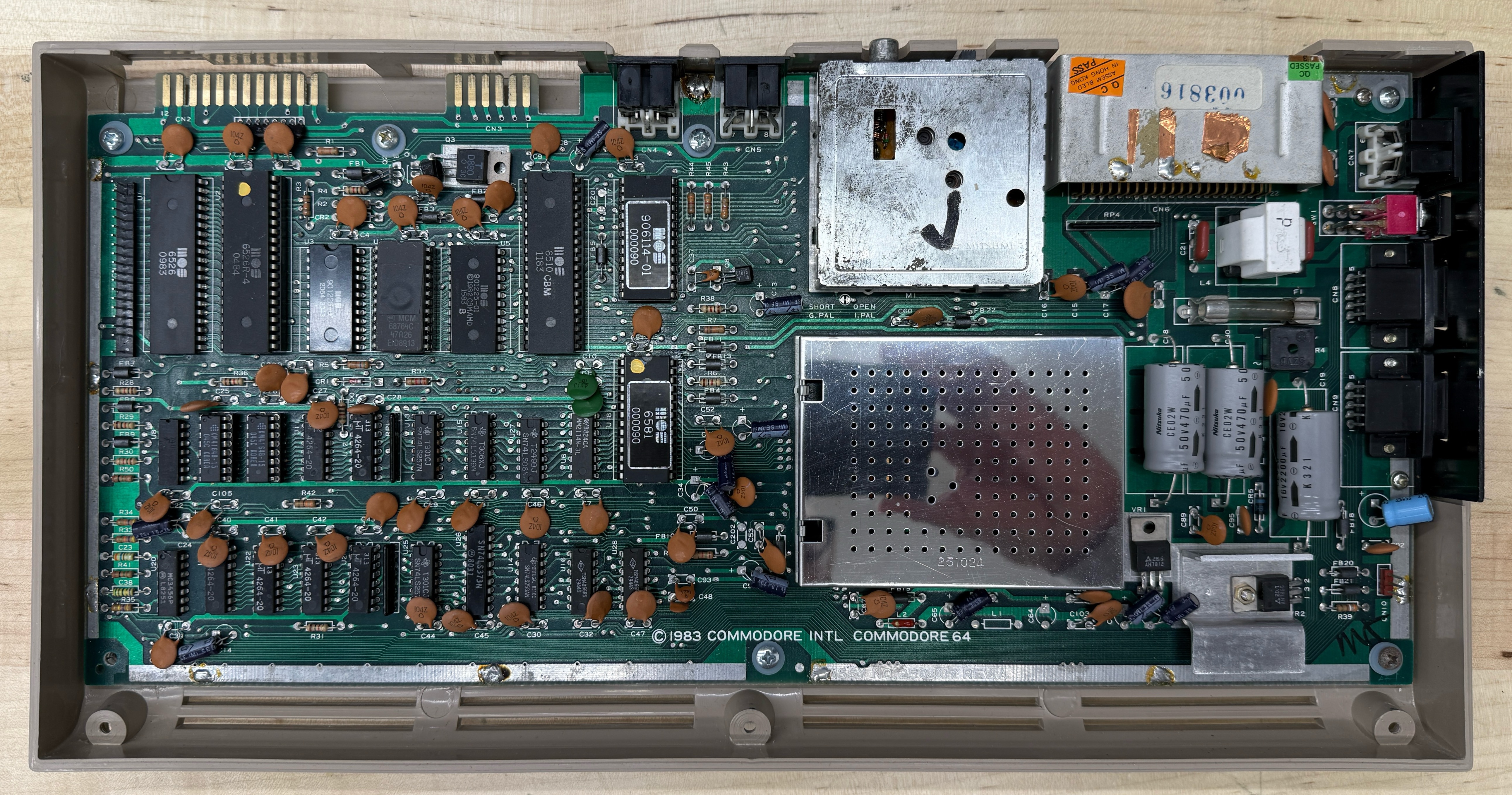 An original 1983 Commodore 64 motherboard in its bottom case shell, top shielding partly visible, before any restoration work