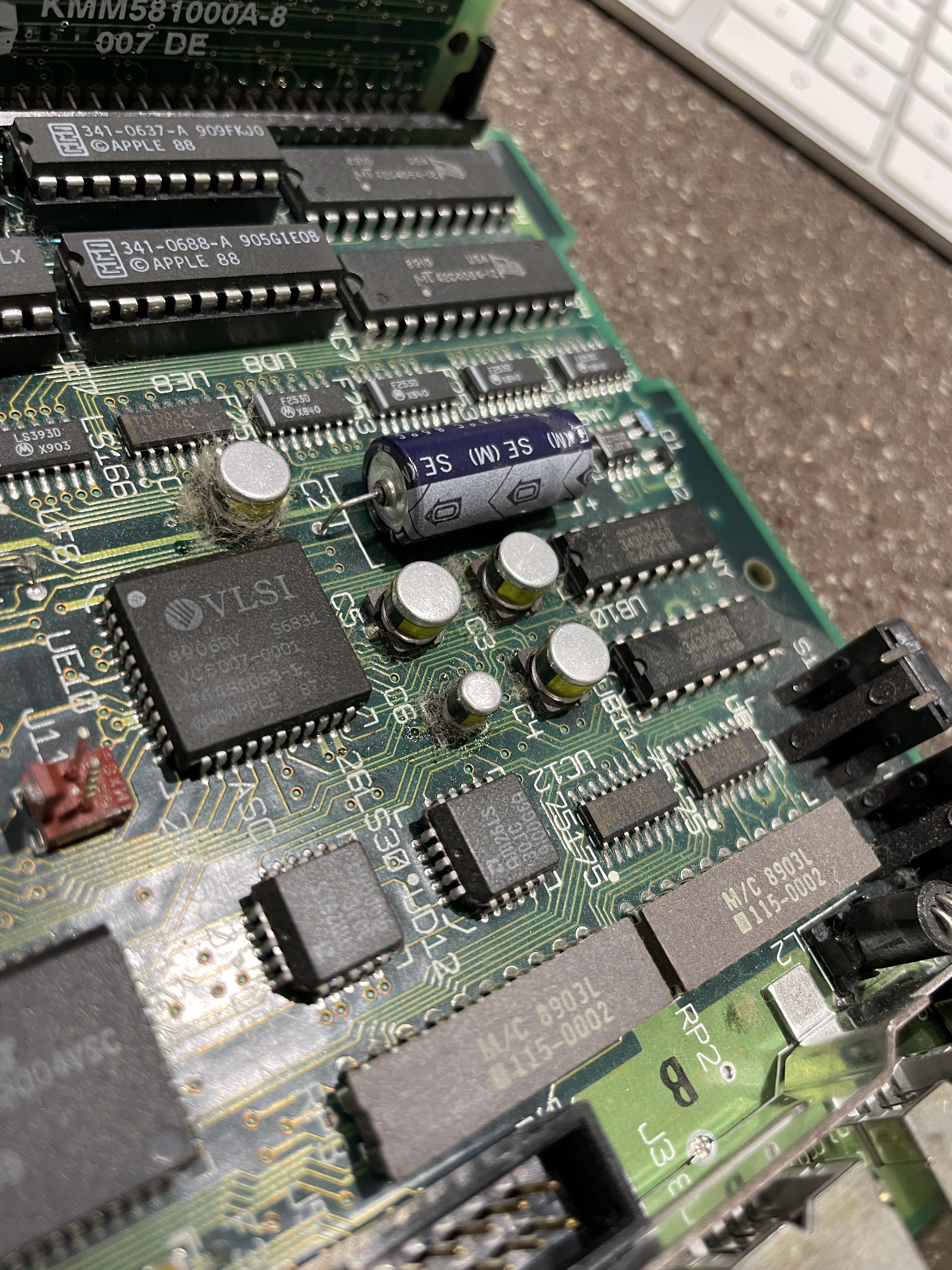 Close-up of the SE/30 logic board showing bulging and leaking surface-mount electrolytic capacitors near the VLSI chip