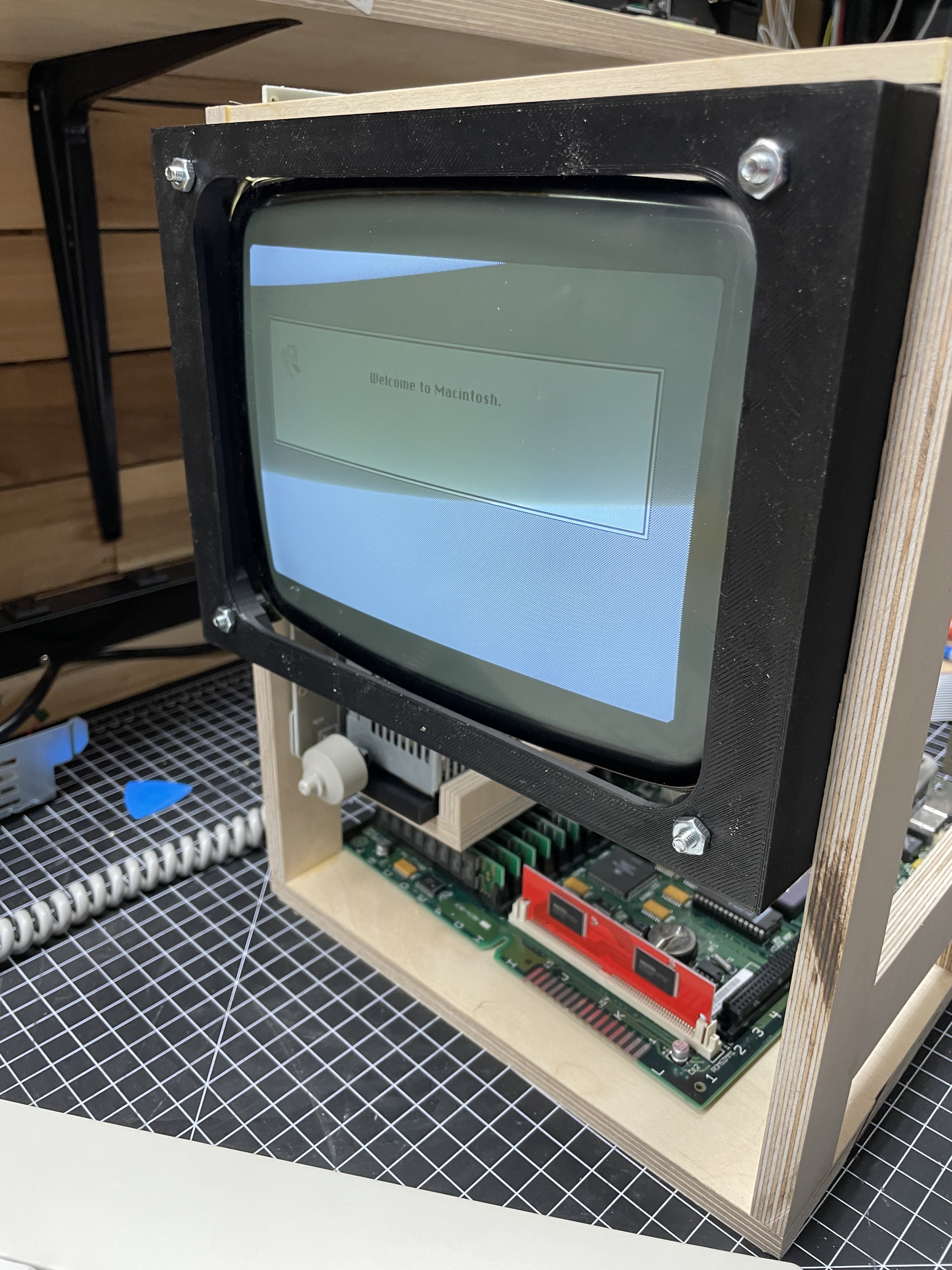 A plywood service jig holding the SE/30 CRT, analog board, and logic board, with the Welcome to Macintosh splash screen visible