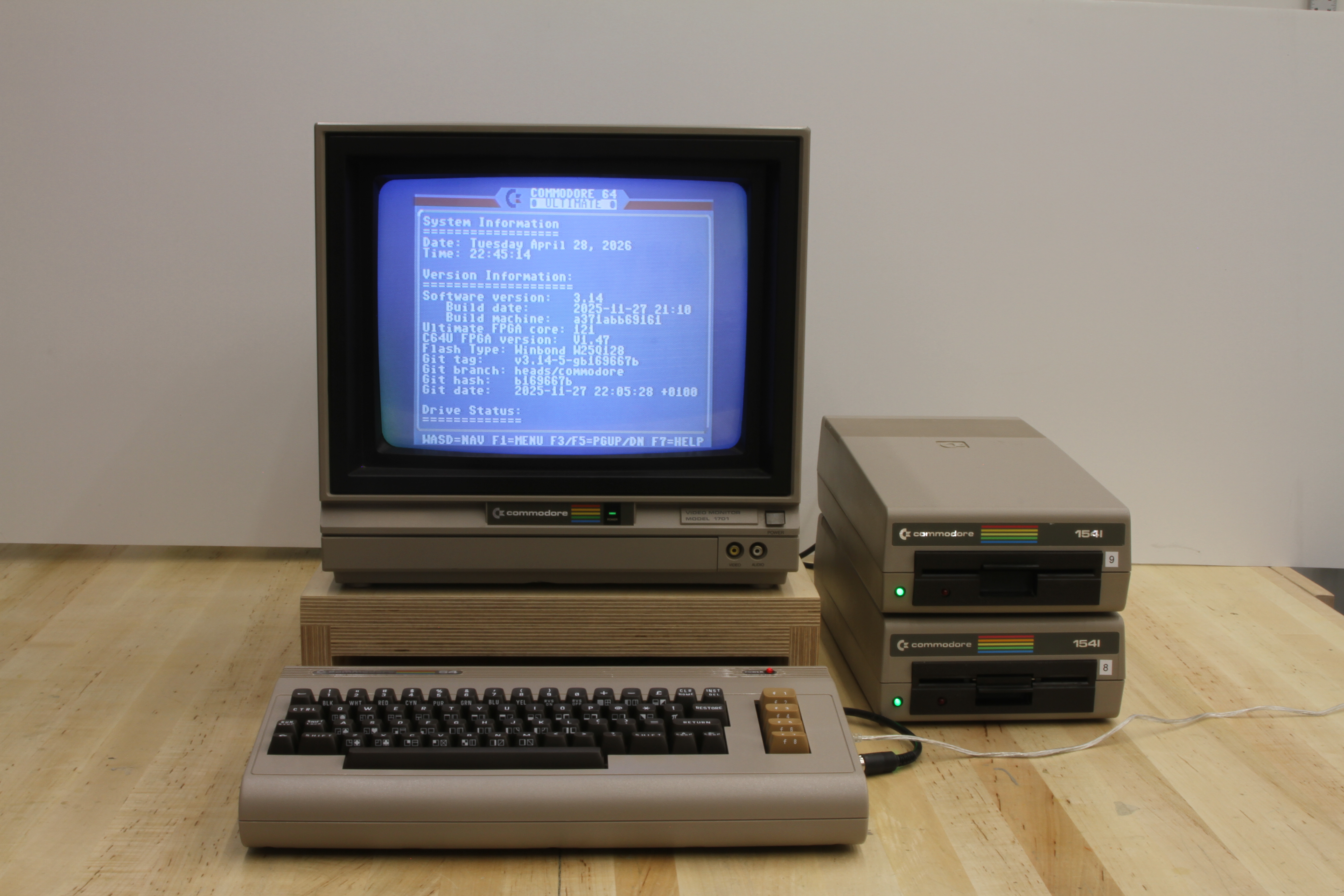 Commodore 64 Ultimate connected to a Commodore 1701 monitor and two stacked 1541 floppy drives, monitor showing the Ultimate's System Information boot screen